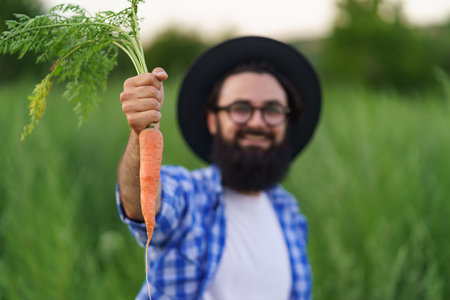 Proud farmer showing his carrots harvest to camera on green field backgroundの写真素材