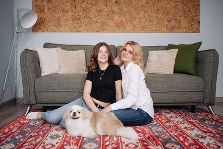 Mother and daughter with dog at home. Portrait of happy girl with dog on rug while mother relaxing at home. Family with petの写真素材
