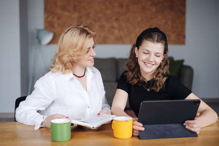 Mother discussing with her daughter teenager while drinking tea in living room at homeの写真素材