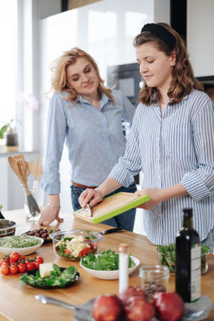 Mom and daughter cooking together in the kitchen. They use vegetables for cooking in a good mood,...