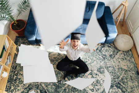 Education, graduation and people concept - top view of happy male student throwing a bunch of sheets...