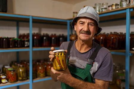 Man satisfied with the result of his work. He holds a glass jar with marinated peppers. Fermented organic food.の写真素材