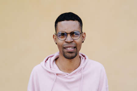 Smiling Afro man portrait wearing pink parka and glasses on pale yellow backgroundの写真素材