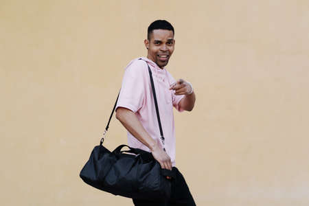 Side portrait of a smiling Afro man with bag walking along pale yellow wall with copy space.の写真素材