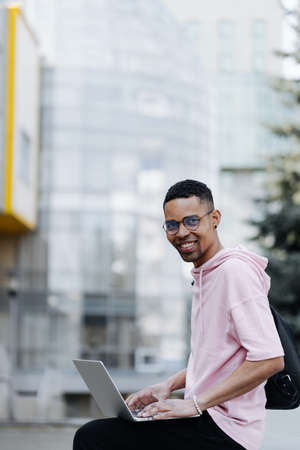 Handsome young man in glasses working on laptop outdoors on a background of corporate buildingの写真素材