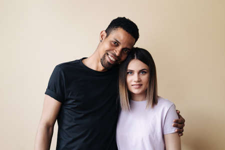 Portrait of happy multiracial couple hugging and posing together over beige background in studio, romantic guy cuddling his afro girlfriendの写真素材