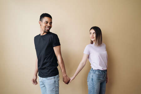 Multiethnic couple holding hands. Young Caucasian woman and African male arms together on beige background. Family conceptの写真素材
