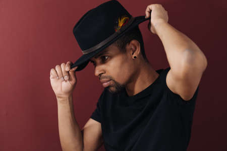 Portrait of handsome young African man smiling in black t-shirt and hat on burgundy background