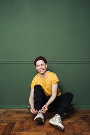 Sporty young Caucasian man dressed in casual wear tying his shoelace against green wall background