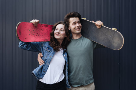 Caucasian skateboarder couple standing together prepare themselves to surf skate on gray wall....