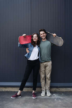 Caucasian skateboarder couple standing together prepare themselves to surf skate on gray wall....