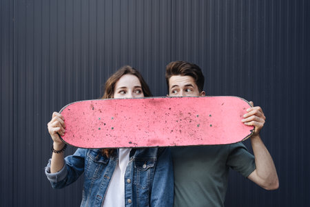 Caucasian skateboarder couple standing together prepare themselves to surf skate on gray wall....