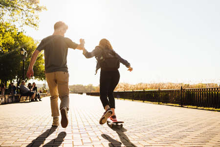 Young Caucasian couple teaching to each others while practicing skating, lifestyle extreme outdoor activity. People lifestyle recreation. Success team skating holding handsの写真素材