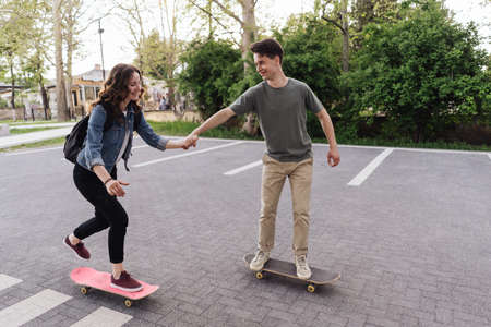 Young Caucasian couple teaching to each others while practicing skating, lifestyle extreme outdoor activity. People lifestyle recreation. Success team skating holding handsの写真素材