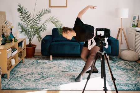 Online ballet classes, teacher explaining motion on camera screen. Young woman teaching ballet using a camera and tripod.の写真素材