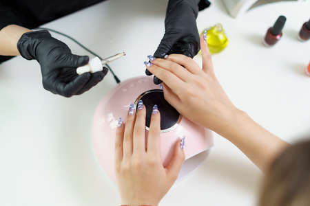 UV lamp gel polish manicure process in a beauty salon. Salon procedure. The master coats the clients nails with a varnish.の写真素材