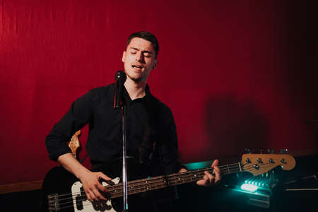 Talented handsome young guitarist man singing a song in studio recording on red background...