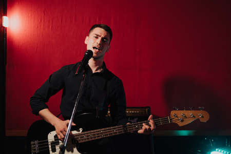 Talented handsome young guitarist man singing a song in studio recording on red background...