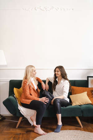 Mother and adult beautiful daughter having fun enjoying talk sit on sofa in modern living room at homeの写真素材