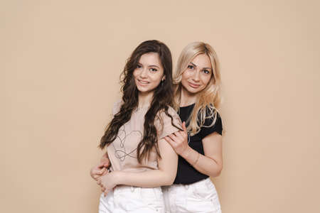 Blonde mother and brunette adult daughter wearing identical clothes, different colors, posing over...