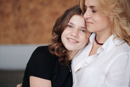 Beautiful mother and her pretty daughter teenager smiling and posing at home.の写真素材
