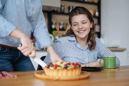 Mom and teen daughter discussing while cutting berries cheesecake, red berries, kiwi, raspberry, strawberryの写真素材
