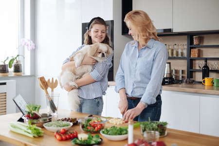 Mom and teen daughter cooking together in the kitchen while daughter coddling their petの写真素材