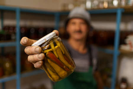 Man satisfied with the result of his work. He holds a glass jar with marinated peppers. Fermented organic food.の写真素材
