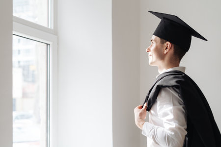 Education, graduation and people concept - happy male student looking in the window to the bright future. Hope, plans conceptの写真素材