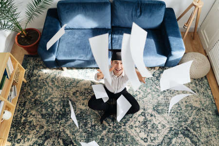 Education, graduation and people concept - top view of happy male student throwing a bunch of sheets...
