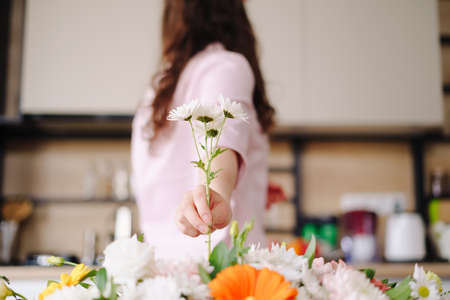 Florist at work: back view of a brunette woman hand arranging last flower in her fashion modern composition at homeの写真素材