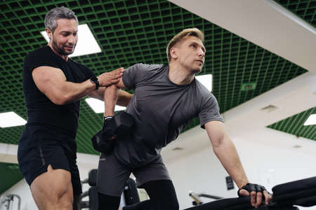 A personal trainer motivates the client to lift heavy dumbbells in the gym. Personal workout hour...