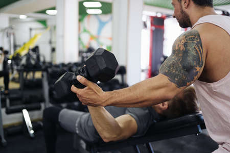 A personal trainer motivates the client to lift heavy dumbbells in the gym. Personal workout hour with personal coachの写真素材