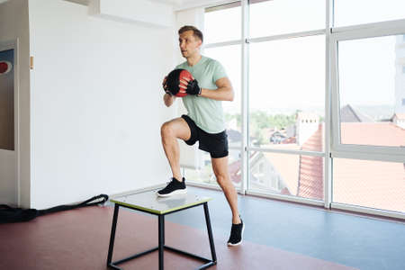 Athlete man working out with ball in the gym with big windows. Caucasian male training CrossFit...