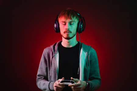 Portrait of gamer playing using a console. Gamer Wearing Headset Standing and holding white console on Dark with red neon lights Backgroundの写真素材