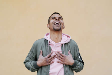 What a lucky guy I am. Shot of man who can not believe in his own happiness, being excited and feeling like on heaver from joy, holding hands on chest, surprised over yellow backgroundの写真素材