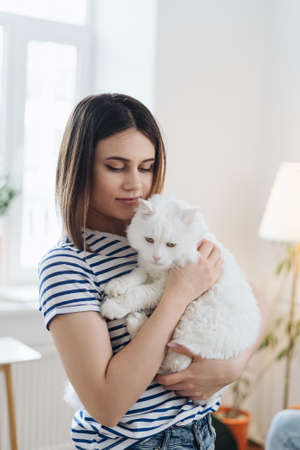Young woman playing with cat in kitchen at home. Girl holding and hugging white cat. Happy master having fun with her petの写真素材