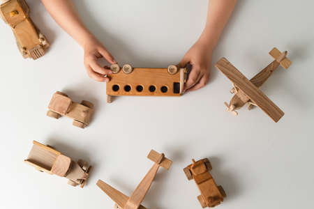 Kid hands playing with wooden toys, bus, plane, cars on white background with blank space for text. Top view, flat lay.の写真素材