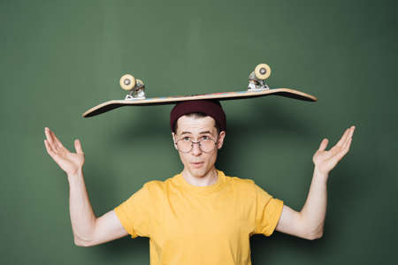 Portrait of young fashionable hipster man posing over green wall background. Caucasian male holding...