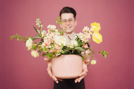 A young man is holding a beautiful bouquet of flowers in his hands on a pink background. The guy decided to make a surprise to his girlfriend. Mothers Day. Womens day. Flowers delivery.の写真素材