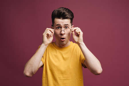 Surprised male, keeps mouth opened, being stupefied as advertises something, wears glasses, yellow t shirt over crimson background. Omg conceptの写真素材