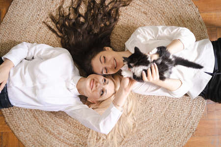 Beautiful blonde mother and lovely brunette daughter lying on round carpet playing with their Kitty catの写真素材