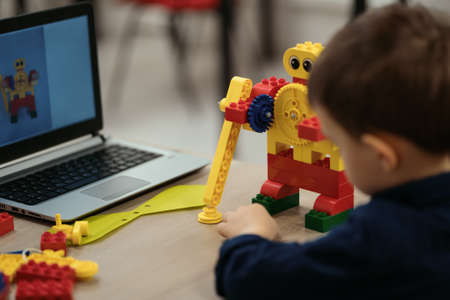 Boy using a laptop to assemble robot from plastic bricks. STEM Education for kids.の写真素材