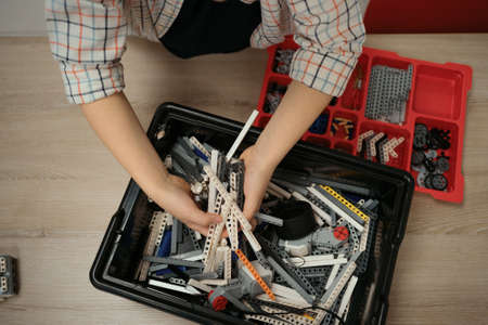 View of hands of incognito kid robot holding elements and working on project, details in box. Colorful pieces from building kit for children on tableの写真素材