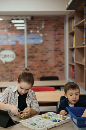 Two kids of different age choose parts of robotic electric toys for building robots at robotics school lesson.の写真素材