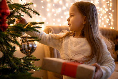 Wondering little girl looking enthusiastic at a decorated fire tree, Led lights and sofa in the backgroundの写真素材