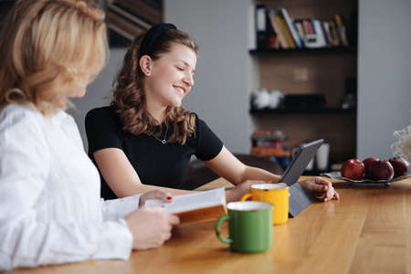 Mother discussing with her daughter teenager while drinking tea in living room at homeの写真素材