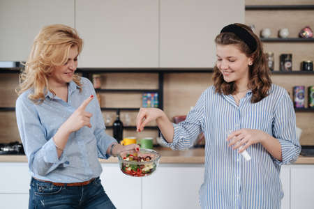 Mom and daughter cooking together in the kitchen. They use vegetables for cooking in a good mood, happy to be togetherの写真素材