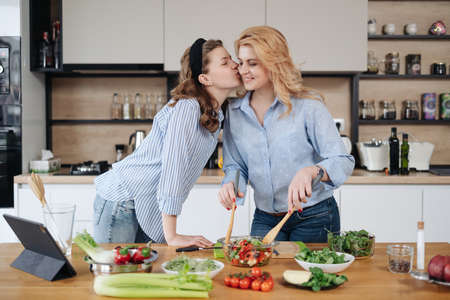 Mom and daughter cooking together in the kitchen. They use vegetables for cooking in a good mood, happy to be togetherの写真素材