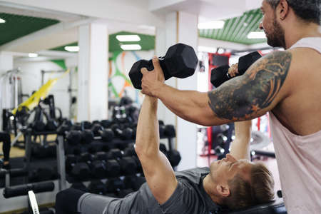 A personal trainer motivates the client to lift heavy dumbbells in the gym. Personal workout hour...